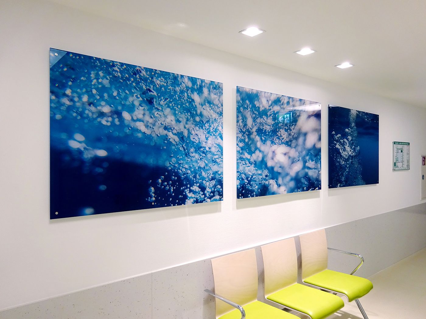 Dreiteiliges Acrylglasbild mit Unterwassermotiv über einer Sitzreihe im Wartebereich einer Praxis