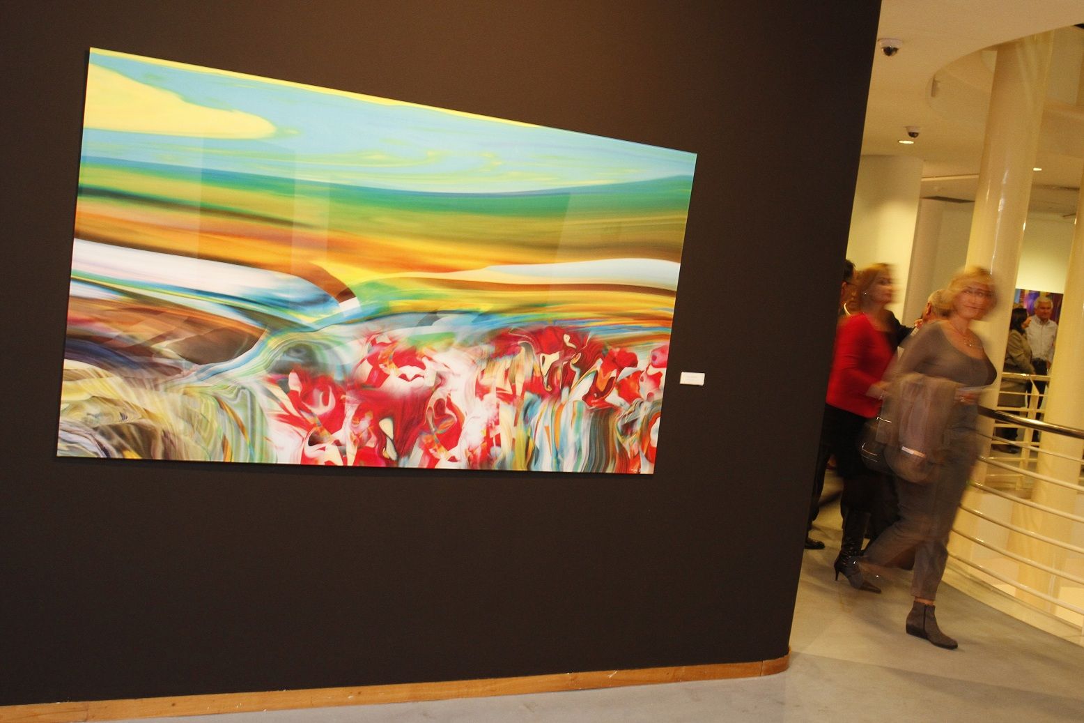 Großformatiges Acrylglasbild an einer dunklen Ausstellungswand während einer Vernissage