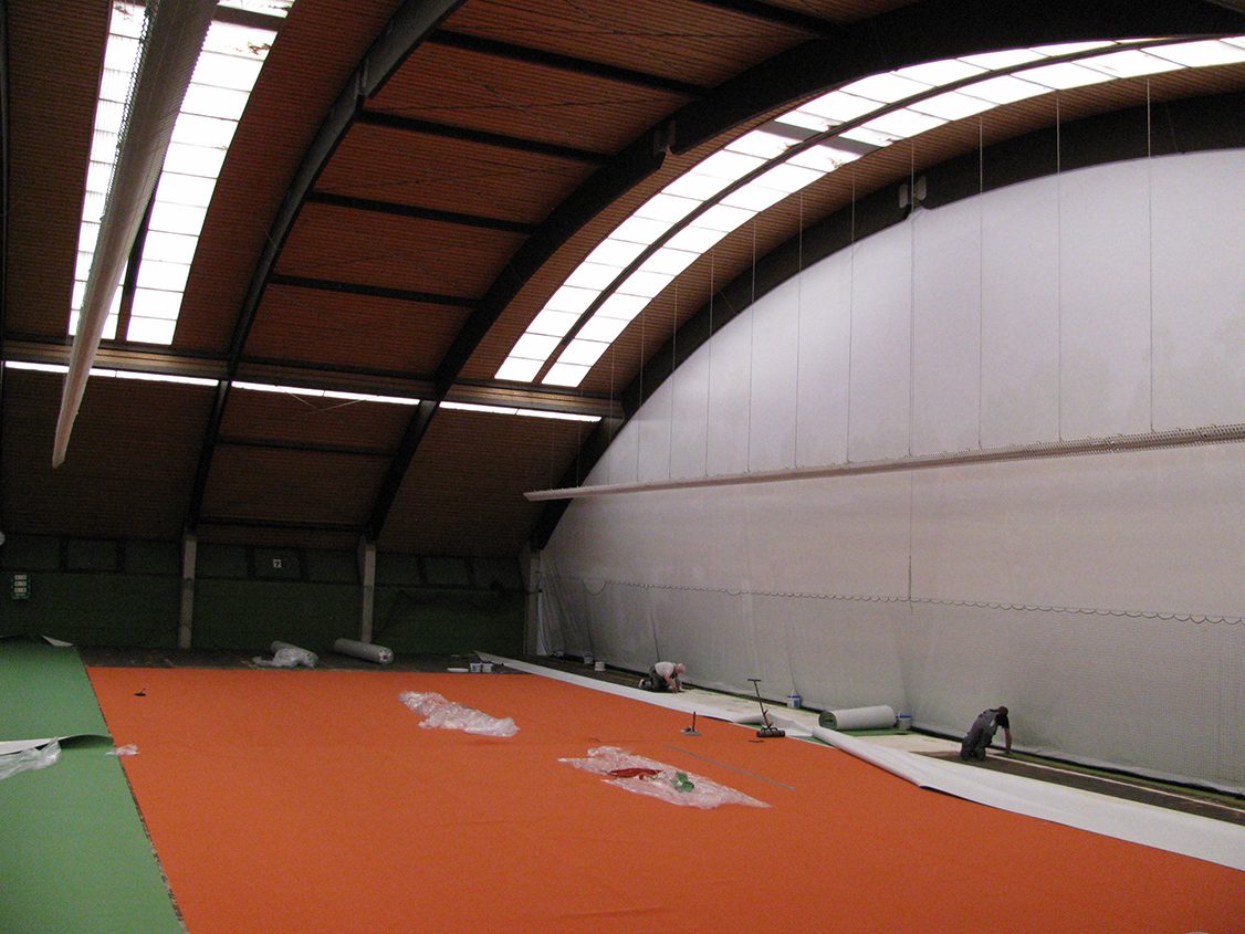 Weiße, von der Hallendecke abgehängte Planen als Raumtrenner in einer Sporthalle während der Bodenverlegung